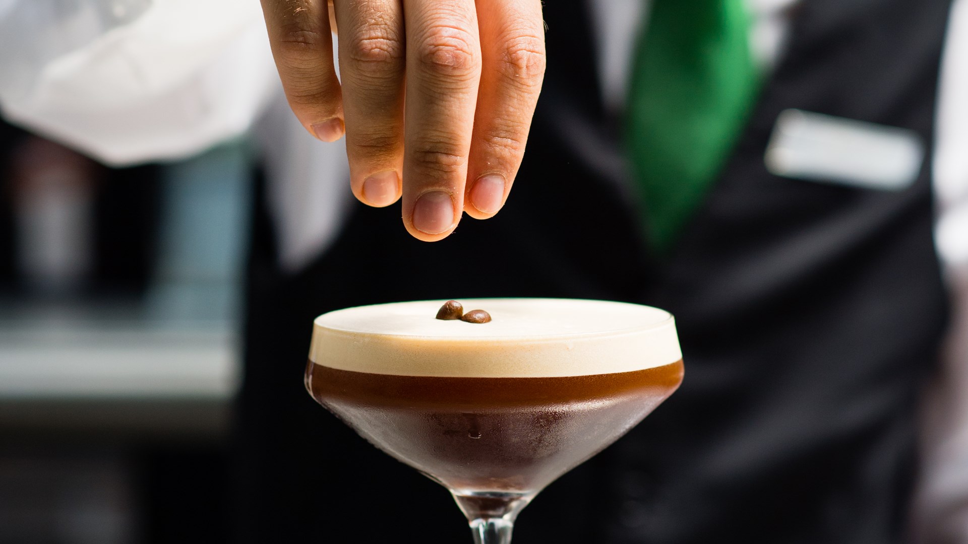 Bartender garnishing an esspresso martini cocktail with coffee beans